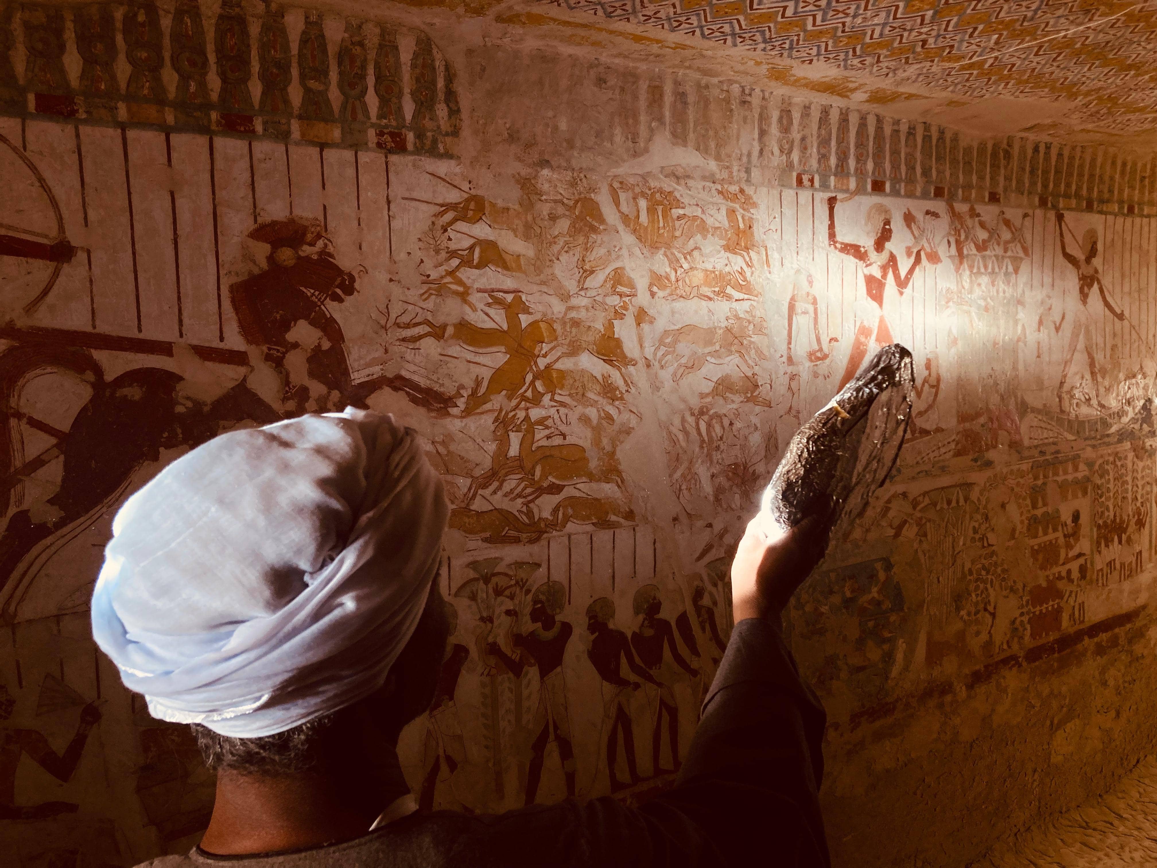 Guía iluminando pinturas funerarias en tumba faraónica